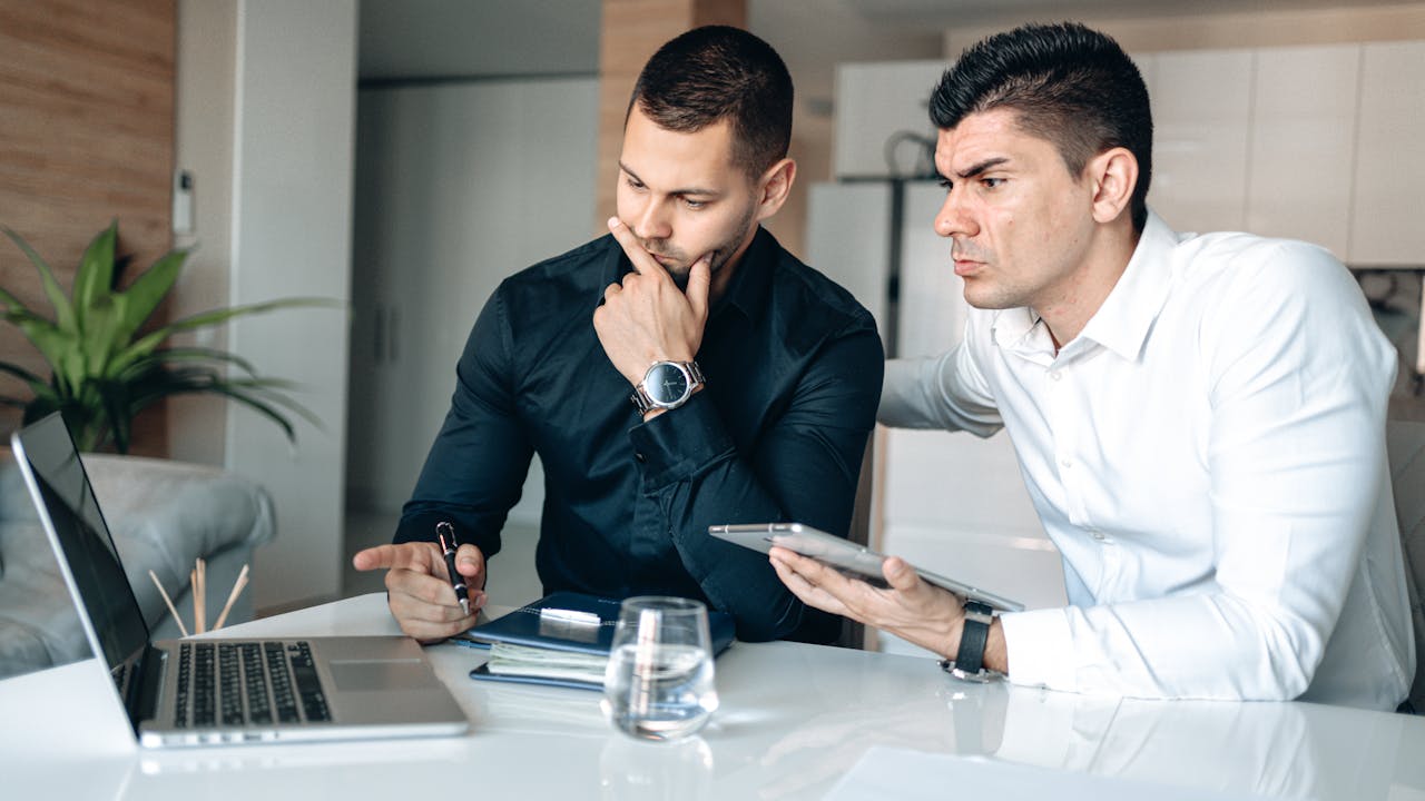 Two businessmen working together with a laptop and tablet in an office setting.